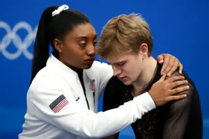 Imagem horizontal mostrando Simone Biles oferece apoio ao patinador Ilia Malinin na Olimpíada de Inverno